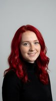 Young Caucasian woman with vibrant red hair wearing black turtleneck sweater smiling at camera against neutral gray background for portrait photography.