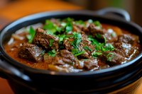 Tender beef chunks slowly cooked in rich brown gravy sauce garnished with fresh herbs, served in traditional black pot. Close up view of hearty stew.
