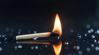 Burning match with bright flame reflecting on dark wet surface with bokeh light effects and water drops creating dramatic atmospheric composition.