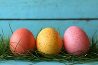 Colorful speckled Easter eggs in coral, yellow and pink shades arranged on fresh green grass against rustic turquoise wooden background, festive spring holiday composition.