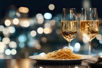 Romantic dinner setting with white wine glasses and pasta dish against blurred city lights bokeh background for fine dining restaurant atmosphere.