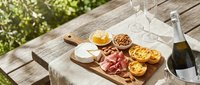 Charcuterie board with cured meats, cheese, crackers and grilled bread arranged on wooden serving platter outdoors with wine for entertaining and gatherings.