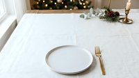 Elegant holiday table setting with white plate, gold fork, and festive greenery decoration on white linen tablecloth for seasonal dining and celebration events.