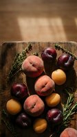 Fresh summer stone fruits peaches plums apricots arranged on rustic wooden cutting board with herbs for healthy organic cooking and food styling.