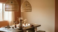 Warm modern dining room with natural wicker pendant lights over wooden table set for breakfast, featuring earth tone decor and soft morning sunlight.