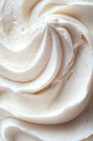 Creamy white meringue or whipped cream swirls in macro close-up showing soft peaks and delicate texture, suitable for dessert and baking backgrounds.