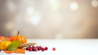 Autumn harvest display with orange pumpkins, colorful leaves and red cranberries on white surface against warm bokeh background for seasonal decorating.