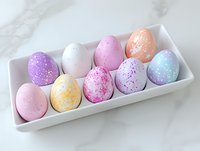 Pastel colored Easter eggs with speckled and dotted patterns arranged in white ceramic dish on marble surface. Festive spring holiday decoration.