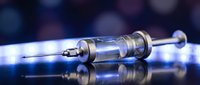 Medical syringe with needle on reflective surface with blue bokeh lights background for healthcare and vaccination concepts.