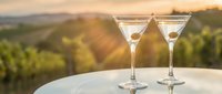 Two elegant martini glasses with olives on white table overlooking vineyard landscape at golden hour sunset for luxury dining and cocktail experiences.