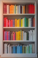 Colorful books arranged in rainbow order on white wooden bookshelf, creating gradient effect from red to blue and green tones. Clean minimal library interior design.