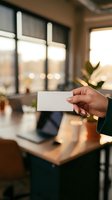 Professional businesswoman holding blank white business card in modern office workspace with warm lighting and blurred background for mockup design.