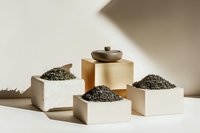 Loose black tea leaves displayed in minimal white ceramic containers and gold pedestal against neutral background with dramatic shadows for food photography.