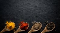 Colorful spices in wooden spoons on dark slate background with copy space for culinary designs and cooking projects.
