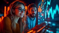 Young Caucasian woman in glasses and orange sweater smiling while analyzing financial market data with male colleague, illuminated by blue trading screens in dark office.