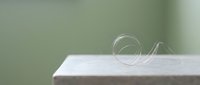 A transparent glass spiral sculpture sits on a white surface against a soft green blurred background, suitable for modern interior design and artistic projects.