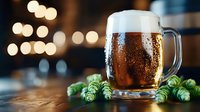 Frosty glass mug of craft beer with fresh green hops and condensation drops on dark wooden table against blurred warm lights background.