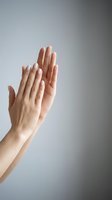 Two female hands with natural manicured nails pressed together in prayer or meditation pose against neutral gray background for wellness and spirituality concepts.