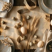 Rustic Easter table setting with quail and chicken eggs, wheat stalks, burlap ribbon and dried flowers on parchment paper for spring holiday decoration.