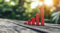 Red ascending arrow graph on wooden surface with blurred green nature background, representing growth, progress, and financial success.