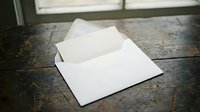 White envelope opened on rustic wooden table surface with natural window lighting creating shadows and vintage atmosphere for correspondence concepts.