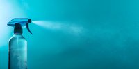 Spray bottle releasing fine mist against turquoise background, demonstrating cleaning product action with dramatic lighting and copy space for text.