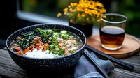 Asian rice bowl with fresh salmon, avocado, seaweed, and sesame seeds served in black ceramic bowl alongside tea on wooden surface, moody food photography.