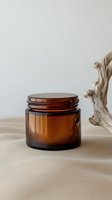 Amber glass cosmetic jar on beige textile with decorative driftwood, minimalist spa composition for natural skincare and wellness products presentation.