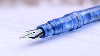 Transparent blue fountain pen with silver nib on white paper background, macro photography showing intricate details and craftsmanship of writing instrument.