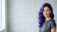 Young woman with vibrant purple wavy hair and warm smile wearing gray t-shirt, standing against neutral white wall with natural light for portrait and lifestyle use.