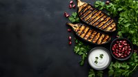 Grilled eggplant slices with charred marks served with fresh parsley, pomegranate seeds and creamy yogurt sauce on dark background with copy space.