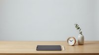 Minimalist workspace with tablet, wooden clock and eucalyptus branch on natural wood desk against neutral wall for productivity and home office design.