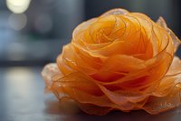 Orange fabric flower with layered petals on blurred background for crafting and decoration projects.