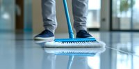 Professional cleaner mopping shiny floor surface in office building. Close-up view of modern blue mop and worker legs in casual wear during cleaning service.