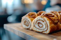 Fresh cinnamon rolls with swirl pattern on wooden cutting board in bakery kitchen with warm bokeh background for breakfast and baking concepts.