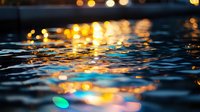 Shimmering water surface with golden bokeh lights reflecting on dark ripples creating magical evening atmosphere. Tranquil nature background for relaxation themes.
