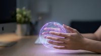 Hands holding glowing purple crystal ball on desk with computer and plant, futuristic technology and fortune telling concept for design projects.