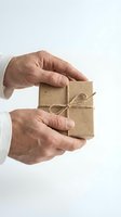 Senior man hands holding small kraft paper gift box tied with natural twine string on white background for holidays and special occasions.