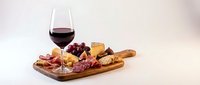 Wine glass with red wine and gourmet charcuterie board featuring assorted cheeses, cured meats, grapes and nuts on wooden serving platter for entertaining.