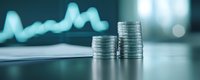 Stacks of silver coins on desk with blurred financial chart graph in background showing business growth and investment success for finance presentations.