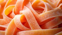 Fresh orange pasta ribbons with dusted flour in macro view, showing delicate texture and curves of homemade fettuccine noodles in warm lighting.