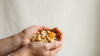 Mixed nuts and dried fruits in cupped hands against neutral background. Suitable for health, nutrition, snacking, and wellness content.