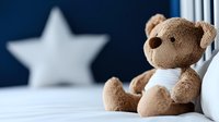 Soft brown teddy bear sitting on white bedding against dark blue wall with decorative star, creating cozy nursery atmosphere for children room decor and bedtime comfort.