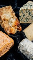 Artisanal cheese selection featuring aged varieties with nuts, blue veins and natural rinds on dark marble surface for gourmet food photography.