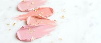 Pink and coral makeup foundation smears with gold flakes on white marble background for cosmetic beauty and skincare advertising campaigns.