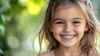 Young girl with bright genuine smile and sparkling eyes against blurred green natural background, radiating joy and innocence in natural outdoor lighting.