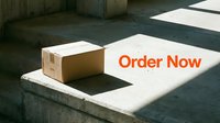 Cardboard delivery box on concrete steps with Order Now text, sunlight and shadows, e-commerce and online shopping concept.