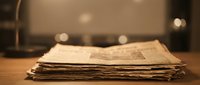 Stack of folded newspapers on wooden table with warm lighting and blurred background for media and journalism concepts.