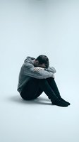 Depressed young man sitting alone with head down showing mental health struggles and emotional pain on white background.