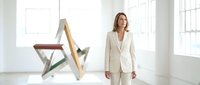 Professional businesswoman in elegant beige suit standing confidently in modern minimalist office space with natural lighting and contemporary furniture.